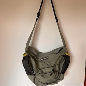 Grön axelväska från iets frans - Grön-grå axelväska från urban outfitters. Använd 2-3 gånger, rymlig och får plats med mycket i de 2 stora facken. Finns innerfickor och ett ytterfack, och även 2 vattenflask hållare. 