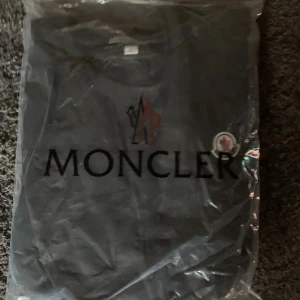 Svart Moncler t-shirt i bomull - Svart t-shirt från Moncler i storlek L med klassisk rund hals och korta ärmar. T-shirten har Moncler-logga broderad på bröstet och är tillverkad i mjuk bomull. Enkel och stilren design som passar perfekt till jeans eller shorts.