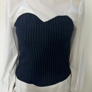 Mörkblå randig korsett med sweetheart - Säljer en mörkblå korsett med tunna vita ränder och snygg sweetheart-urringning. Toppen har en figurnära passform och stängs med dragkedja bak. 