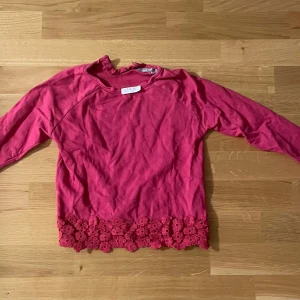 Rosa långärmad tröja med blommig spets - Superfin rosa långärmad tröja från Sweet Me med rund hals och dekorativ blommig spetskant nertill. Perfekt för dig som gillar söta detaljer och vill ha något som sticker ut lite extra. Mjuk och skön bomullskvalitet.