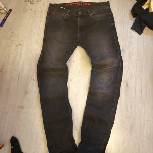 Svarta Hugo 708 skinny jeans - Snygga svarta jeans från Hugo, modell 708, med skinny passform och klassisk femficksdesign. Jeansen har röda detaljer vid fickorna och ett rött Hugo-märke baktill i midjan. Materialet är stretchigt jeans och midjan är normal.