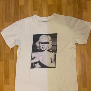 Vit t-shirt med tryck - Vit t-shirt från OneWear med ett stort svartvitt tryck på framsidan föreställande en ikonisk kvinna med texten 'society' över ögonen. Klassisk passform och rund halsringning. Perfekt för dig som gillar statement-plagg.