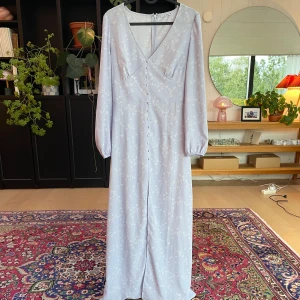 Ljuslila långklänning Nelly x Glamorous - En ljuslilla klänning. En väldigt fin klänning med vita blommor med en liten slits. Säljer denna för att kläningen var fel storlek för mig! Hör gärna av dig om fler frågor och intressen💕