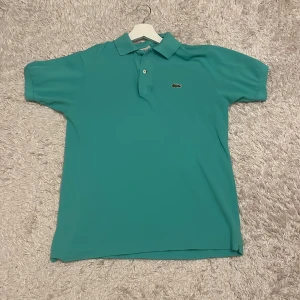 Lacoste pike - Säljer min Lacoste piké som jag inte använder. Det är en knäpp som är borta men de är den längst uppe så det är inte så viktigt. Färgen är turkos