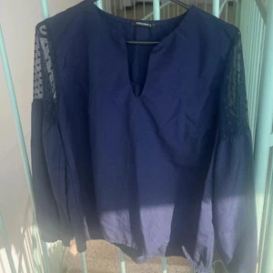 Marinblå blus med spetsärmar  - Snygg marinblå blus  med v-ringning och långa ärmar i spetsdetaljer. Blusen har en lös passform och är perfekt för dig som gillar stilrena plagg med en twist. Ärmarna har diskreta prickar i spetsen för extra detalj.