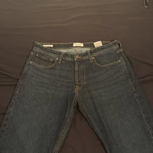 Mörkblå jeans från Jack & Jones - Säljer ett par klassiska mörkblå jeans från Jack & Jones med raka ben och snygga kontrastsömmar. Jeansen har fem fickor, bälteshällor och en läderpatch bak i midjan. Perfekta för en chill och stilren look.