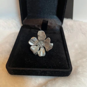 Silverfärgad blomring med diamanter  - Unik ring i silverfärg med stor blomformad design och små gnistrande kristaller i mitten. Blomman har detaljerade blad och ringen är justerbar för perfekt passform. Perfekt statement piece för dig som vill sticka ut. Rostfri 💝