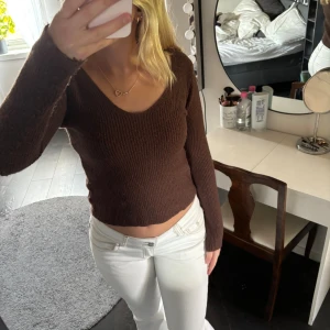 Brun stickad croppad tröja - Mysig brun stickad tröja med croppad passform och v-ringad hals. Tröjan har långa ärmar och är perfekt för lager-på-lager under kyligare dagar. Enkel och stilren design som passar till det mesta.