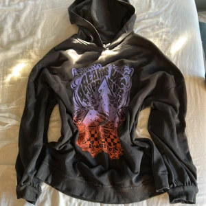 Svart hoodie med tryck från Divided H&M - Cool svart hoodie från Divided H&M med färgstarkt tryck i lila och orange framtill. Oversized passform, mjukt fleecetyg på insidan och klassisk huva. Perfekt för dig som gillar streetstyle och unika prints.