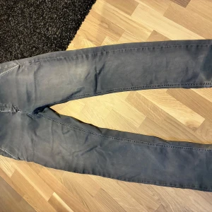 Grå byxor från Replay W28 - Snygga grå kostymbyxor från Replay med raka ben och klassiska fickor bak med knappar. Byxorna har bälteshällor och är tillverkade i ett mjukt bomullsmaterial. Perfekta för en clean och stilren look.