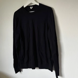 Mörkblå ulltröja från Arket, storlek L - En stilren mörkblå långärmad tröja från Arket i storlek L. Tillverkad i mjuk ull, perfekt för lager-på-lager och passar till allt. Klassisk rund halsringning och ribbade muddar för en clean look. 2H19