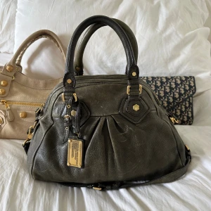 Mörkgrön Q Classic Aidan bag! - Perfekta skolväskan! Stilren och rymlig mörkgrön Marc by Marc Jacobs Classic Q Aidan i äkta läder med guldfärgade detaljer och dubbla handtag. Långa bandet finns. Den höga och eleganta formen gör att den rymmer en 13” MacBook tillsammans med allt du behöver för skola, jobb eller fritid. Finns slitage på lädret som syns på bilderna.  Väskan har dragkedja upptill och praktiska innerfack för smidig organisering. Kan bäras i handen eller på axeln. En eftertraktad Q-Classic väska.  Mått ca 26×36×14