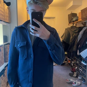 Mörkblå overshirt från Zara - Säljer en stilren mörkblå overshirt från Zara. Jackan har två stora bröstfickor med lock och knappar, klassisk krage och knäppning framtill. Materialet är bomull och modellen är normal i passformen. Perfekt att slänga på över en t-shirt eller hoodie