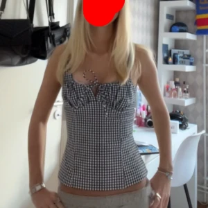 Rutig svartvit linnetopp med knyt - Supersöt linnetopp i svartvitt rutigt mönster med smala axelband och knyt framtill. Toppen är figurnära och har en lätt rynkad detalj vid bysten. Perfekt för varma dagar och enkel att styla med jeans eller kjol.