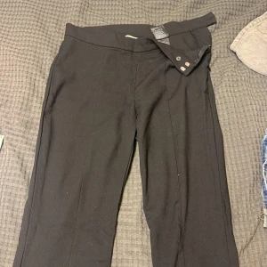 Svarta kostymbyxor med slits - Svarta kostymbyxor med snygg slits nertill på benen. Byxorna har en klassisk rak passform och stängs med knapp och dragkedja. Perfekta för en stilren look och tillverkade i ett mjukt tyg som känns bekvämt hela dagen.