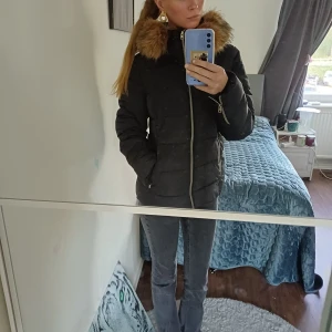 Svart pufferjacka med fuskpäls - Säljer en svart pufferjacka med mysig huva som har fuskpäls i brunt. Jackan har dragkedja framtill och på fickorna. Perfekt för kyliga dagar och riktigt snygg. I en av fickorna är det HÅL men det går säkert att fixa. Skriv för fler frågor eller bilder. Storlek 40, men passar även om du har storlek S 