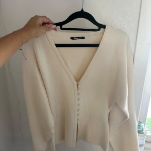 Beige kofta från Gina Tricot - Superfin beige kofta från Gina Tricot med v-ringning och snygga tygklädda knappar framtill. Koftan är i mjukt stickat material och har långa ärmar. Perfekt att slänga över en topp för en chill och stilren look. Den är endast använd en gång så i nytt skick! 