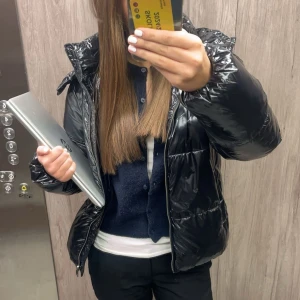 Svart glansig pufferjacka med huva - Säljer en svart glansig pufferjacka med huva och dragkedja. Jackan har en oversized passform och är vadderad för extra värme. Perfekt för kalla dagar och har en modern look som passar till många outfits😍