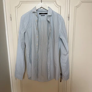 Randig skjorta från Tiger of Sweden - Snygg skjorta från Tiger of Sweden i slim fit med ljusblå och vita vertikala ränder. Perfekt för en clean och stilren look.