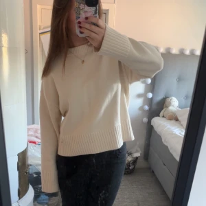 Beige stickad tröja med breda muddar - Säljer en beige stickad tröja med breda ribbade muddar vid ärmslut och nederkant. Tröjan har en avslappnad passform och är långärmad, perfekt för lager på lager under kyligare dagar.