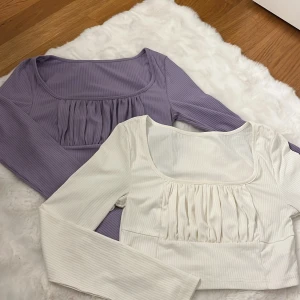 Ribbad topp med rynk från SHEIN storlek M - Två långärmade ribbade toppar från SHEIN i storlek M. En är vit och en är ljuslila, båda med fyrkantig ringning och rynkade detaljer framtill. Tillverkade i stretchig polyesterblandning för en bekväm passform. Perfekta att styla med jeans eller kjol.