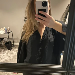 Svart blus  - Säljer en svart blus från h&m med v-ringning och vida ärmar. Blusen har en snygg pärlknapp vid ärmslutet som extra detalj. Tyvärr har ena knappen gått av men det finns medföljande extra knapp som man enkelt kan sy på!! Passar s/m