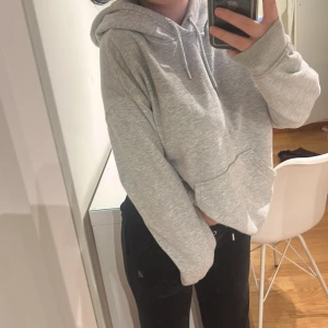 Grå hoodie med huva och ficka - Säljer en grå hoodie med huva och snörning. Tröjan har en stor magficka och är i mjukt bomullsmaterial. Perfekt för chill dagar och har en relaxed, oversized passform med långa ärmar.