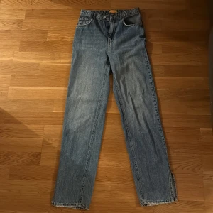 Blå raka jeans från Gina Tricot - Klassiska blå jeans från Gina Tricot med rak passform och normal midja. Jeansen har fyra fickor, dragkedja och knapp framtill samt råa kanter nertill på benen för en avslappnad vibe. Perfekta till sneakers eller boots.