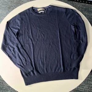 Mörkblå kashmirblandad tröja Nano & Co - Mörkblå rundhalsad tröja från Nano & Co i kashmirblandning. Tröjan har ribbade muddar vid ärmslut och nederkant, samt en klassisk och stilren look. Perfekt för dig som gillar en enkel men snygg stil.