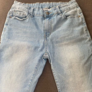 Ljusblå jeans från D.M.D By denim day - Säljer ett par ljusblå jeans från D.M.D By denim day i storlek 158. Klassisk femficksmodell med resår i midjan och knappstängning. Jeansen har raka ben och är tillverkade i mjukt denimtyg som är skönt att bära hela dagen.
