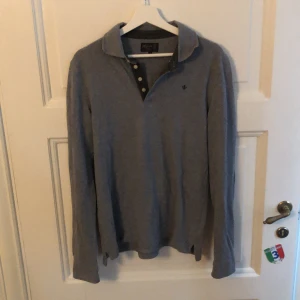 Grå pikétröja från Morris, storlek M - grå långärmad pikétröja från Morris med klassisk krage och knappar framtill. Broderad logga på bröstet och diskret design som passar till många stilar. Skön bomullskvalitet och stilren look.