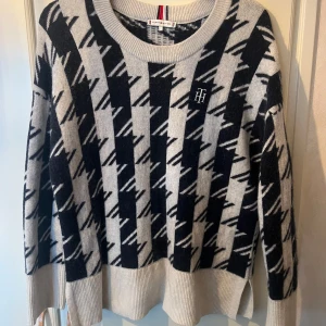 Rutig stickad tröja Tommy Hilfiger - Snygg stickad tröja från Tommy Hilfiger i grått och svart med rutigt mönster. Tröjan har rund halsringning, ribbade muddar och TH-logga broderad på bröstet. Perfekt för dig som gillar klassisk men trendig stil. Helt ny! Nypris var 2000kr