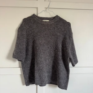 Brun stickad tröja från Gina Tricot - Mysig brun stickad tröja från Gina Tricot med korta ärmar och rund halsringning. Tröjan har en lite boxig passform och är tillverkad i ett mjukt ullblandat material som passar perfekt för lager-på-lager under kyliga dagar.