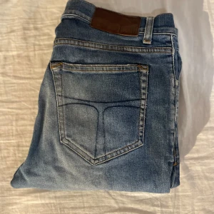 Blåa tiger of sweden - Snygga blå tiger of sweden jeans med klassisk femficksdesign och läderpatch bak i midjan. Jeansen har en något tvättad look med ljusare partier och raka ben. Perfekta för en avslappnad stil och passar till det mesta.