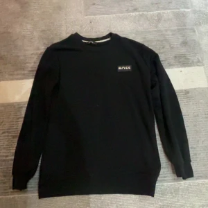 Svart sweatshirt från BOSS, storlek S - Svart sweatshirt från BOSS i klassisk modell med rund hals och lång ärm. På bröstet sitter en snygg BOSS-logga i svart, vitt och orange. Tröjan är i mjuk bomull och har ribbade muddar vid ärmslut och nederkant. Perfekt för en clean och stilren look.jag har satt på mig den men inte använt den 
