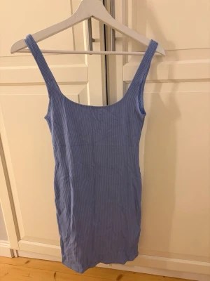 Blå ribbad kortklänning Pull&Bear - Supersnygg blå ribbad kortklänning från Pull&Bear. Klänningen har breda axelband, figurnära passform och är tillverkad i ett stretchigt material som känns bekvämt. Perfekt för sommardagar eller när du vill ha en enkel men stilren look.