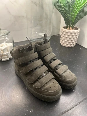 Nike Air Force 1 mocka sneakers - Säljer ett par mörkgröna Nike Air Force 1 sneakers i mocka med högt skaft. Skorna har flera kardborreband över vristen, snörning och perforerad tå. Klassisk Nike-logga på hälen och sidan. Riktigt chunky och street-inspirerad look.
