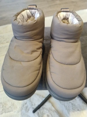 Helt nya Beige vinterboots från UGG 36 - Säljer ett par Helt Nya beige vinterboots från UGG med fluffigt foder och vadderad ovandel.Storlek 36. Skorna har en rejäl sula med UGG-logga undertill och är perfekta för kalla dagar. Insidan är fodrad med mjukt material för extra värme och komfort. priset kan diskuteras 