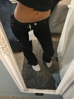 Svarta bootcut jeans från Gina Tricot - Säljer ett par svarta jeans från Gina Tricot med bootcut-snitt och låg midja. Jeansen har klassisk femficksdesign, silverfärgad knapp och dragkedja framtill. Materialet är jeans och passformen är loose. Perfekt för dig som gillar en avslappnad stil.