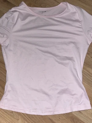 Ljusrosa t-shirt från SHEIN - Enkel och stilren ljusrosa t-shirt från SHEIN med rund hals och korta ärmar. Tillverkad i mjukt material som känns skönt mot huden. Perfekt att matcha med jeans eller kjol för en clean look.