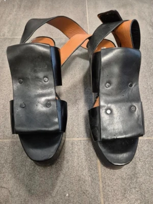 Svarta platåskor/sandaletter i läder 36 - Unika svarta sandaletter från & Other Stories i äkta skinn. Skorna har breda remmar och fyrkantig tå, samt en rejäl platåsula och klack. Snyggt minimalistisk design. Perfekta för dig som gillar statement-skor och vill sticka ut.