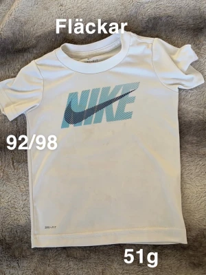 Vit Nike t-shirt med blå logga - Säljer en vit t-shirt från Nike med stor blå logga. Klassisk rund hals och korta ärmar, perfekt för aktiva dagar.🌸Fläckar. Storlek 92/98