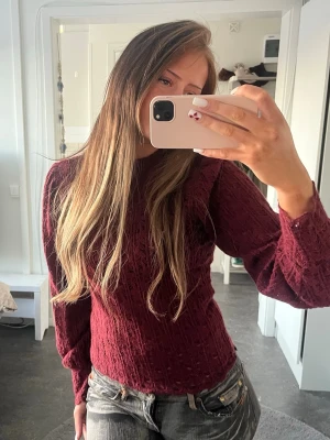 Vinröd spetsblus med lång ärm - Vinröd blus i spets med lång ärm och hög hals. Blusen har ett fint mönster, vågig kant nertill och sitter figurnära. Använd fåtal gånger