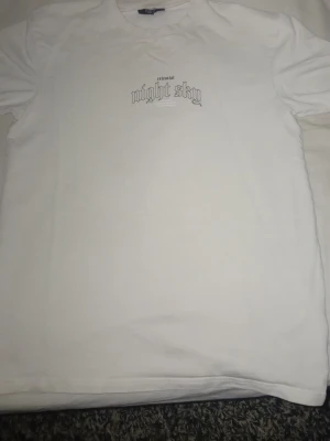 Vit t-shirt med tryck 'night sky' - Säljer en vit t-shirt med trycket 'celestial night sky' i svart på både bröstet och ryggen. T-shirten har klassisk passform och rund hals. Materialet känns som bomull och trycket ger en clean och stilren vibe.