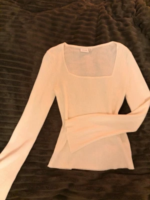 Vit ribbad topp, Vila - Säljer en vit långärmad topp från Vila i storlek S. Toppen har en snygg fyrkantig halsringning och är ribbad i materialet vilket ger en cool struktur. Passformen är slim och ärmarna är långa. Perfekt att styla med jeans eller kjol.