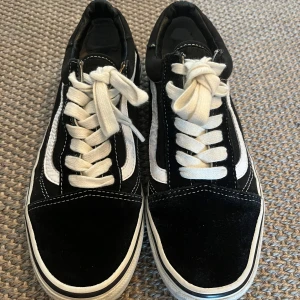 Svarta och vita Vans Old Skool sneakers - Klassiska Vans Old Skool sneakers i svart och vitt med vit sula och den ikoniska sicksack-randen på sidan. Skorna har snörning, rund tå och ovandel i canvas och mocka. Yttersulan är i gummi med det klassiska rutmönstret. Perfekta för en avslappnad streetstil.