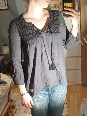 Grå Odd Molly blus - En blusacktig Odd Molly tröja med 3/4 ärmar i mörkgrått med brodering och knyte både vid brösted och i ärmarna. Gjord i 100% bomull.