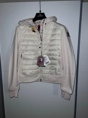 Parajumpers cardigan vit/beige - Finns i alla storlekar XS-XXL                             Snygg ljusbeige pufferjacka från Parajumpers med quiltad front, huva och dragkedja. Kommer med original påse och prislappar.