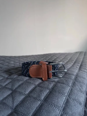 Svart grått blått flätat bälte - Tja det är helt nytt från Bältgallerian. Det är 105cm långt och 3,5cm brett. Det är i ett elastiskt material så passar större storlekar också. Om du inte gillar den här färgen så finns det många flera att välja mellan. Vid köp av bundle så blir kostnaden billigare.