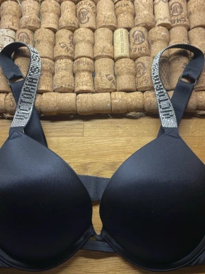 Svart push-up bh Victoria's Secret - SOM NY!!!    Snygg svart push-up bh från Victoria's Secret med glittriga axelband där det står 'Victoria's Secret' i stenar.som ny och säljer för att den är för liten 